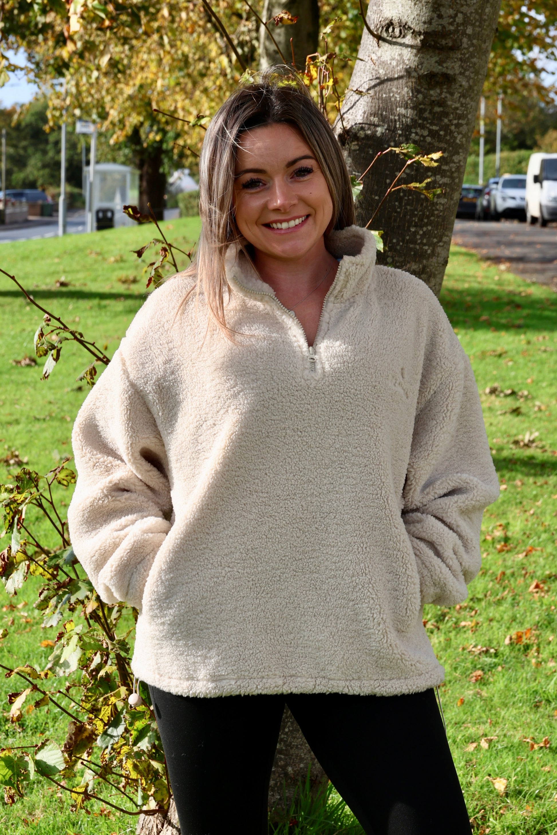 Woman wearing a beige sweater standing outdoors near a tree