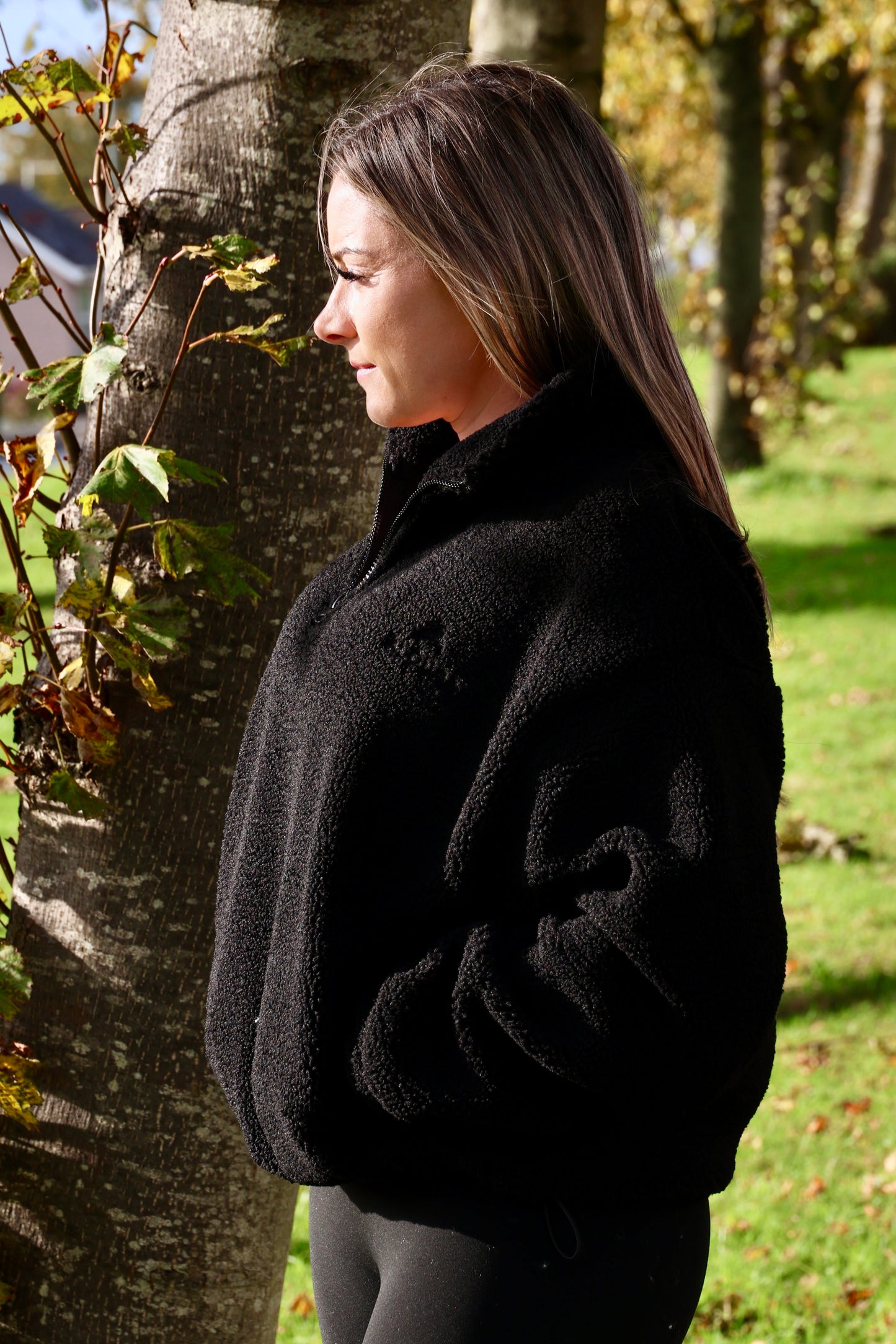 Woman wearing a black coat standing next to a tree in an outdoor setting