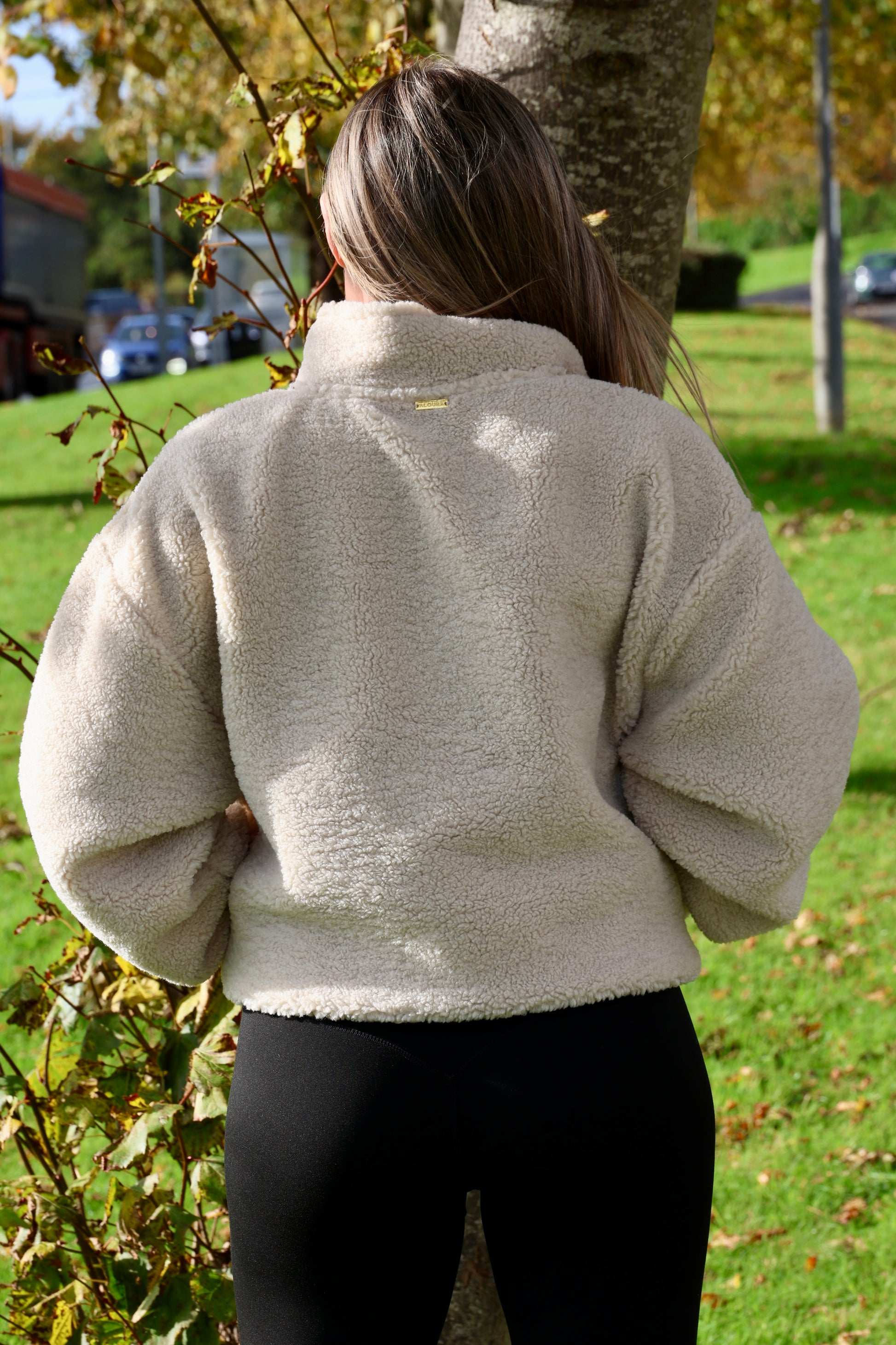 Person wearing a beige fleece jacket standing outdoors with trees and grass in the background