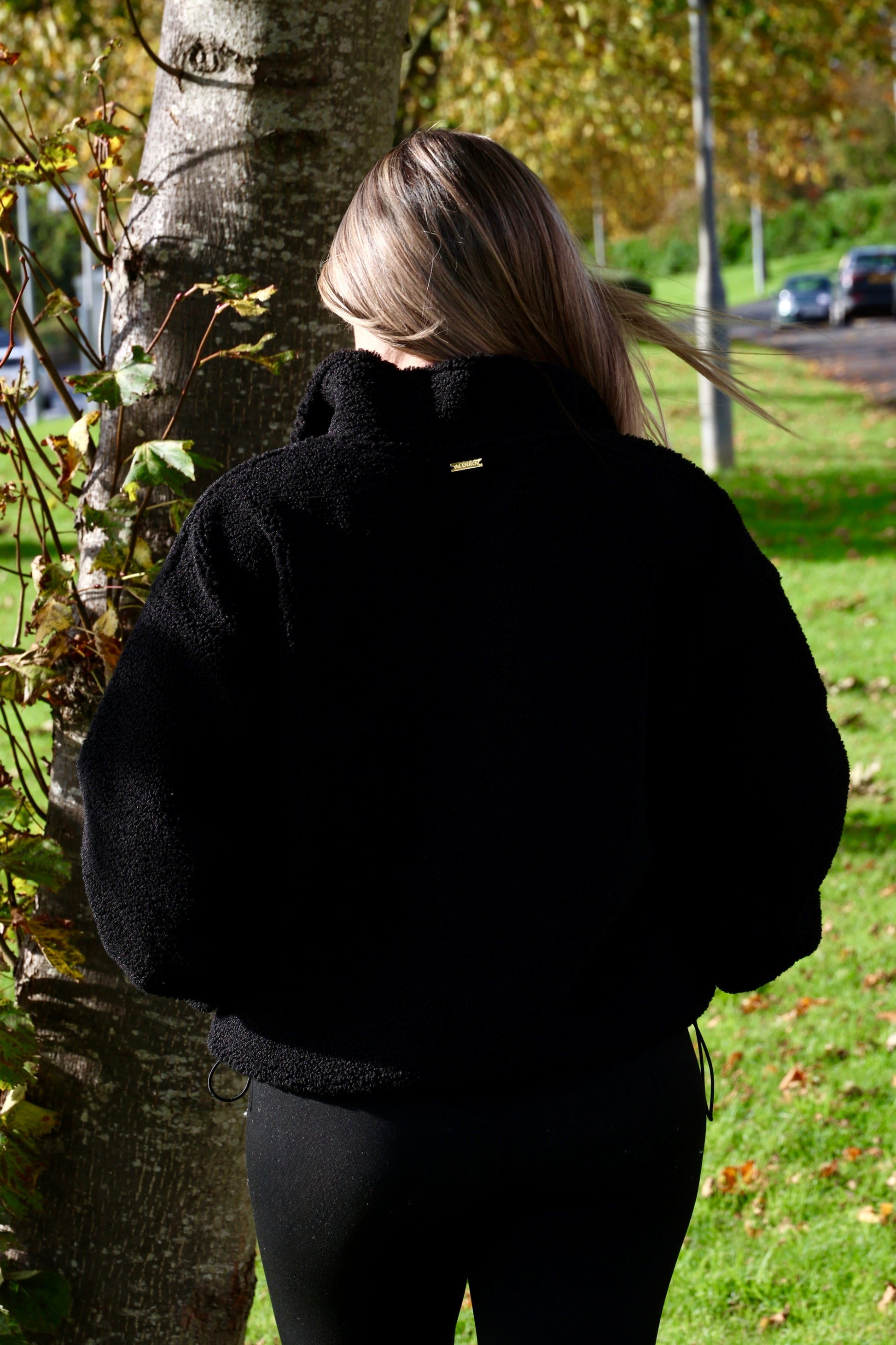 Person wearing a black jacket standing outdoors near a tree